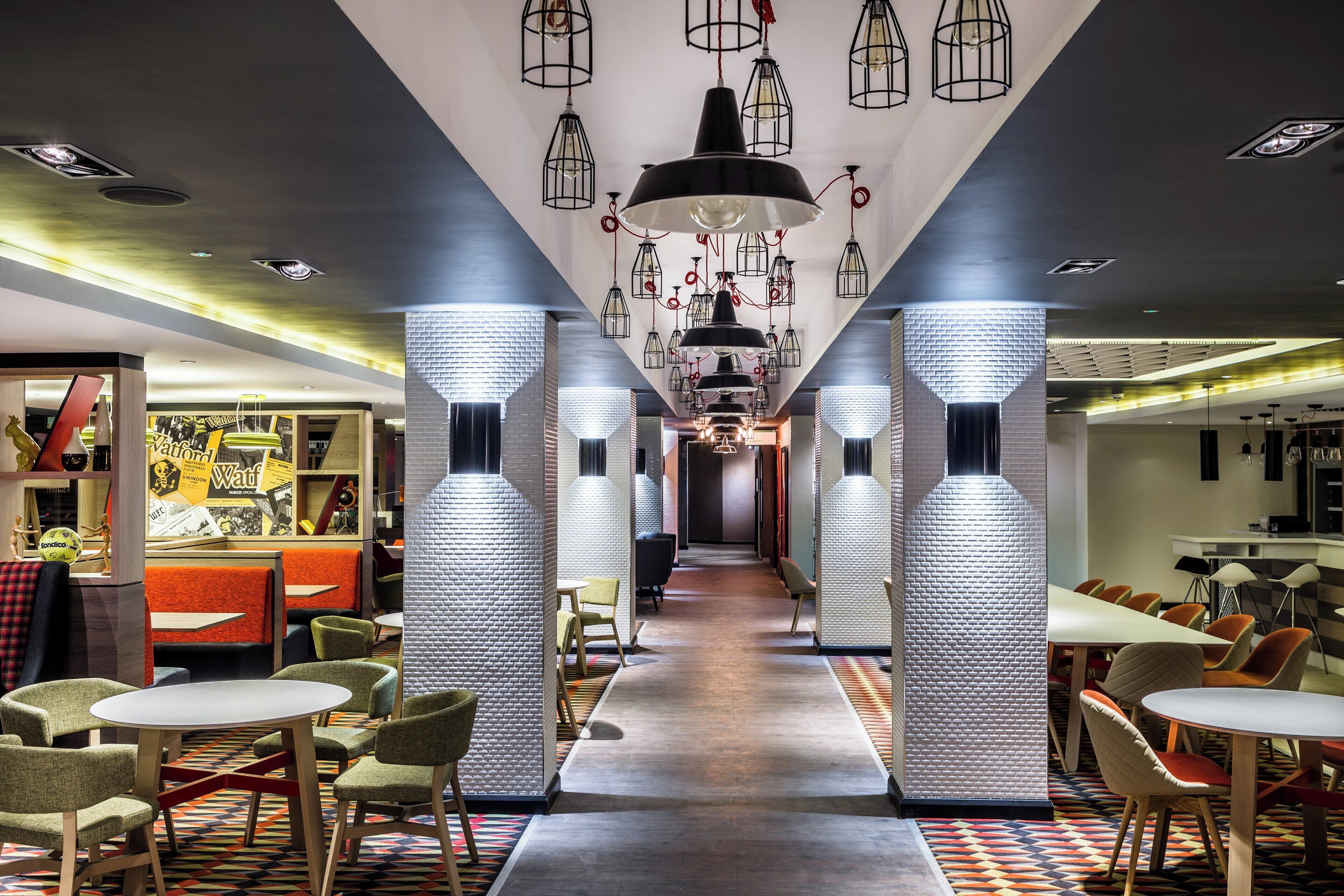 A modern hotel lobby with a central walkway, seating areas, and a bar on the left.
