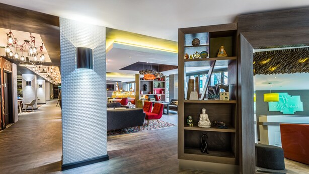 A modern interior with a central column, a seating area with red chairs, and a bookshelf with various items.