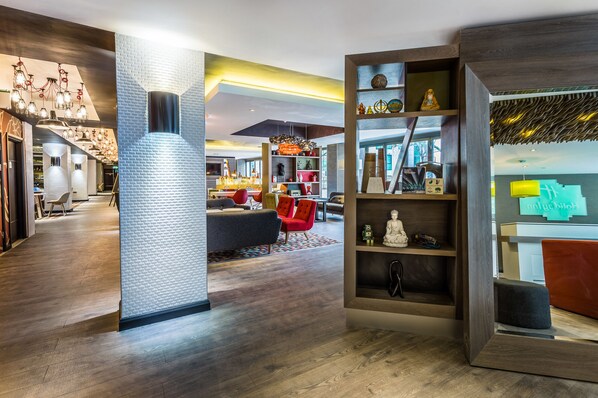 A modern interior with a central column, a seating area with red chairs, and a bookshelf with various items. - Holiday Inn London - Watford Junction by IHG (Watford)