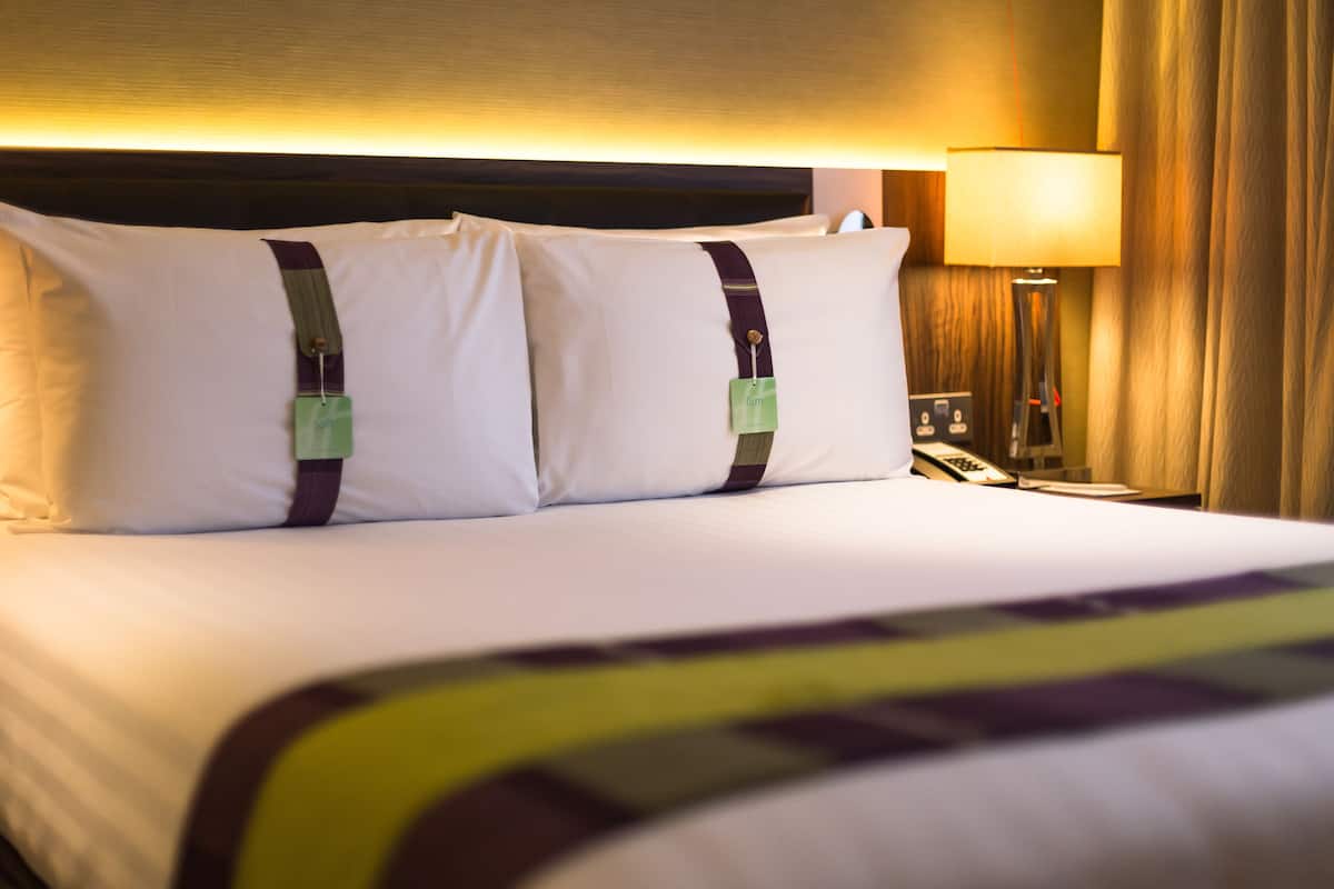 A hotel room with a neatly made bed, a nightstand with a lamp, and a wooden headboard.