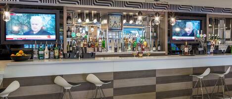 A bar area with multiple televisions displaying news, a variety of liquor bottles, and bar stools.