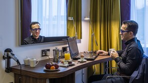 A hotel room with a desk, laptop, coffee cup, and breakfast items.