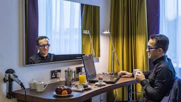 A hotel room with a desk, laptop, coffee cup, and breakfast items.