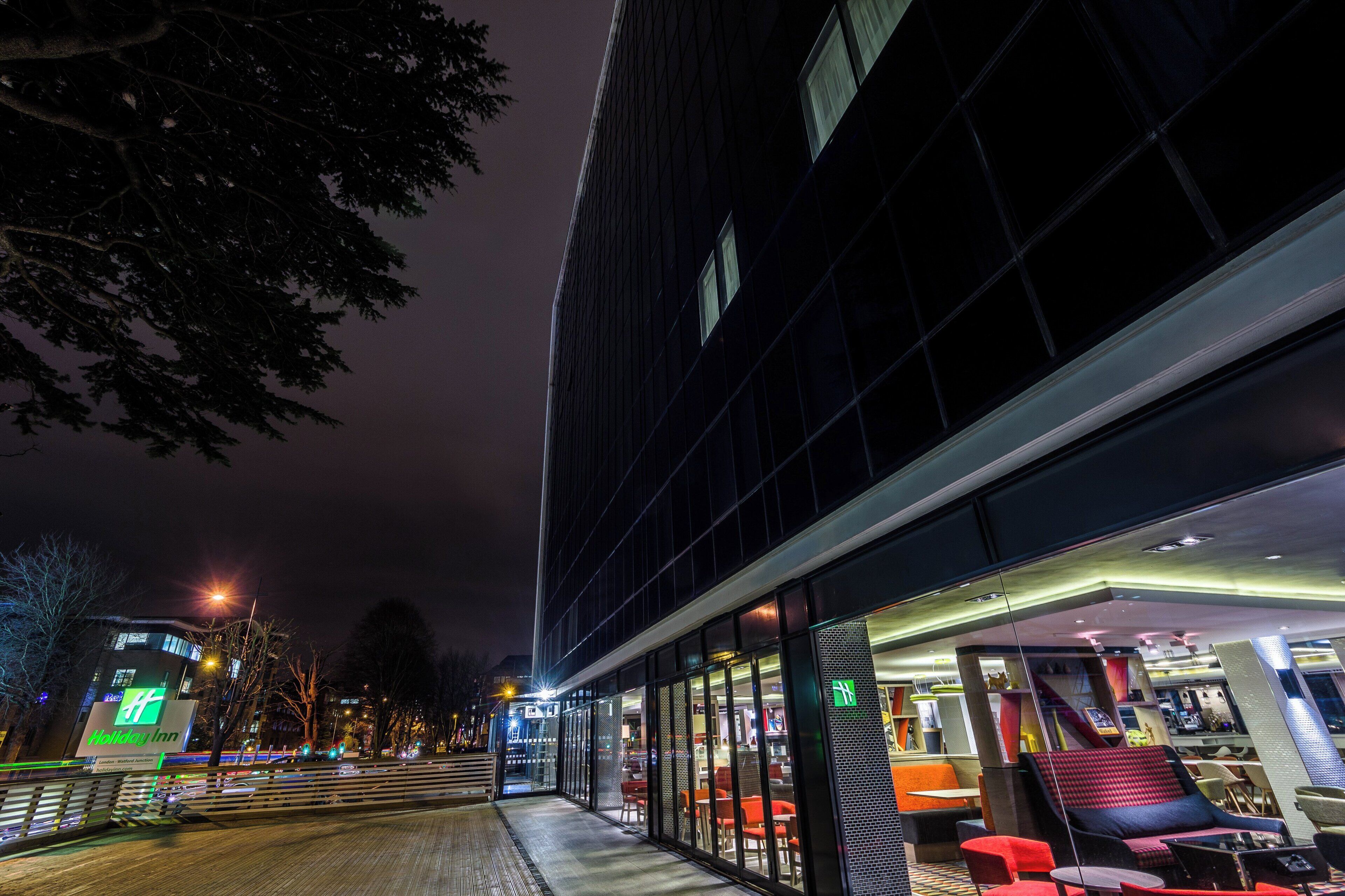 En moderne bygning med en glasfacade, udendørs siddeområde og et Holiday Inn skilt.