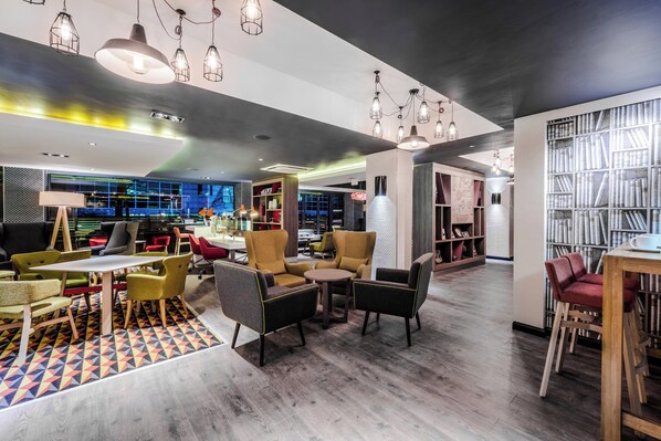 A modern lounge area with seating, tables, and a bookshelf.