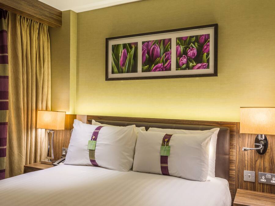 Habitación de hotel con una cama grande, dos lámparas de noche, un cuadro enmarcado de flores y un cabecero de madera.