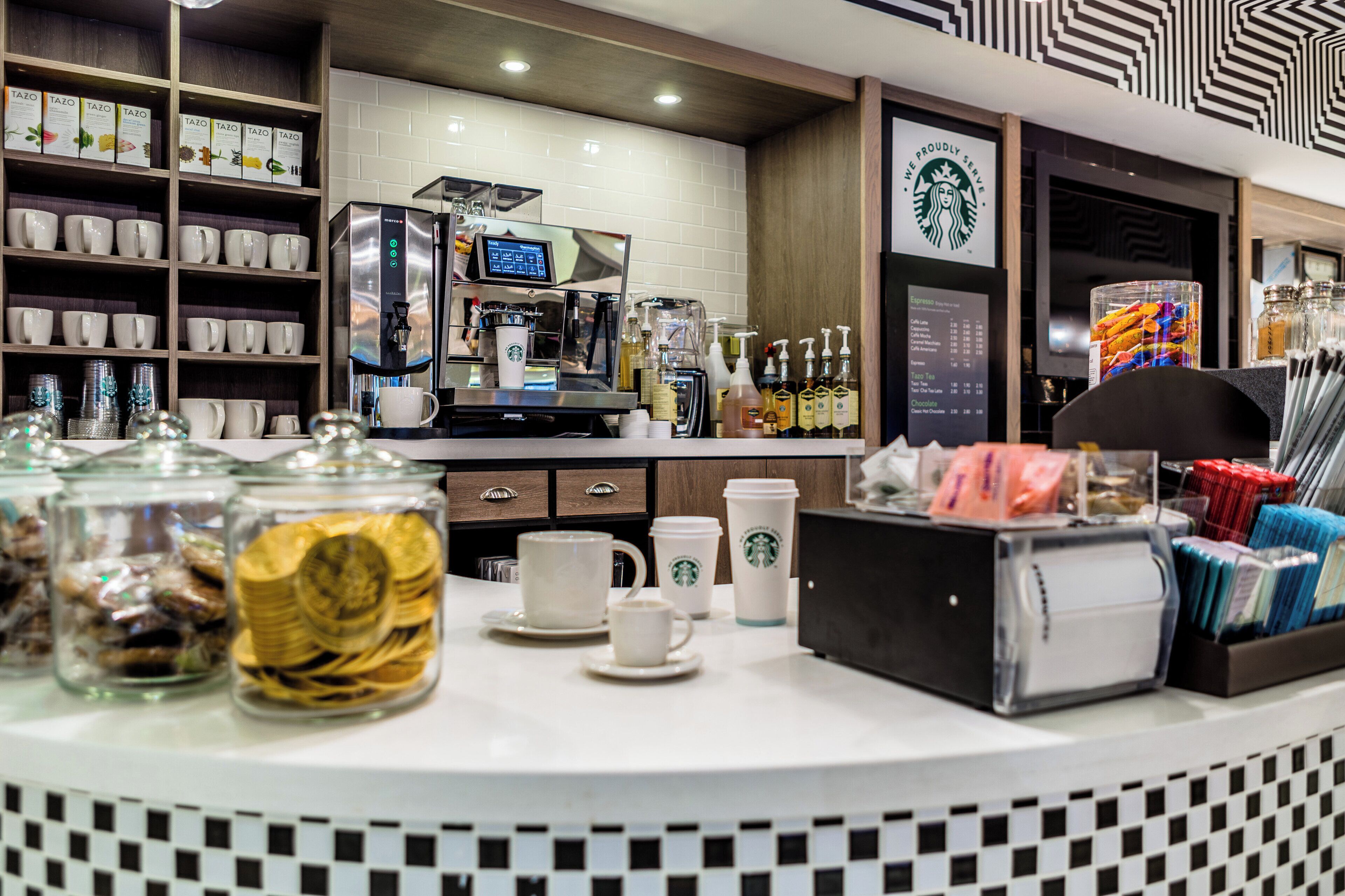 A coffee shop counter with a coffee machine, cups, and a menu board.