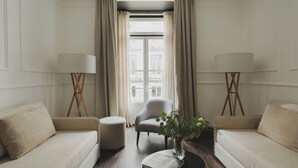 Habitación de hotel con dos sofás, una mesa de centro redonda, una silla y dos lámparas de pie.
