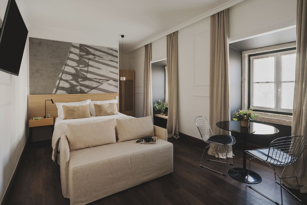 Een moderne hotelkamer met een groot bed, een bank, een bureau met stoel, een televisie en een raam met gordijnen.