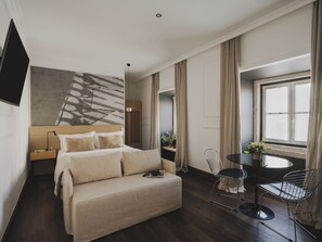 Quarto de hotel moderno com uma cama grande, um sofá, uma escrivaninha com cadeira, televisão e janela com cortinas.