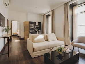Un salon moderne avec un canapé, une table basse et un coin repas, la cuisine étant visible au fond.