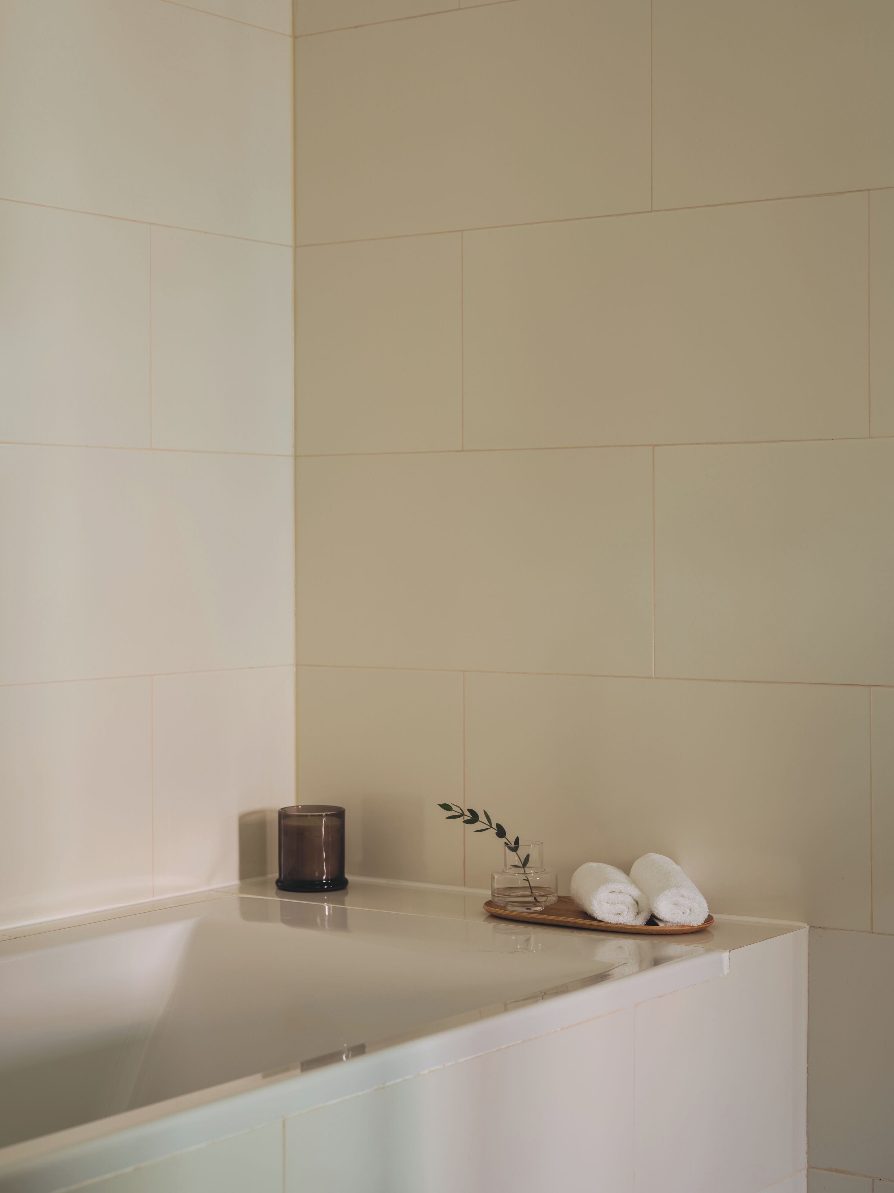A bathroom with a bathtub, a small glass container with a plant, and two rolled towels on a tray.