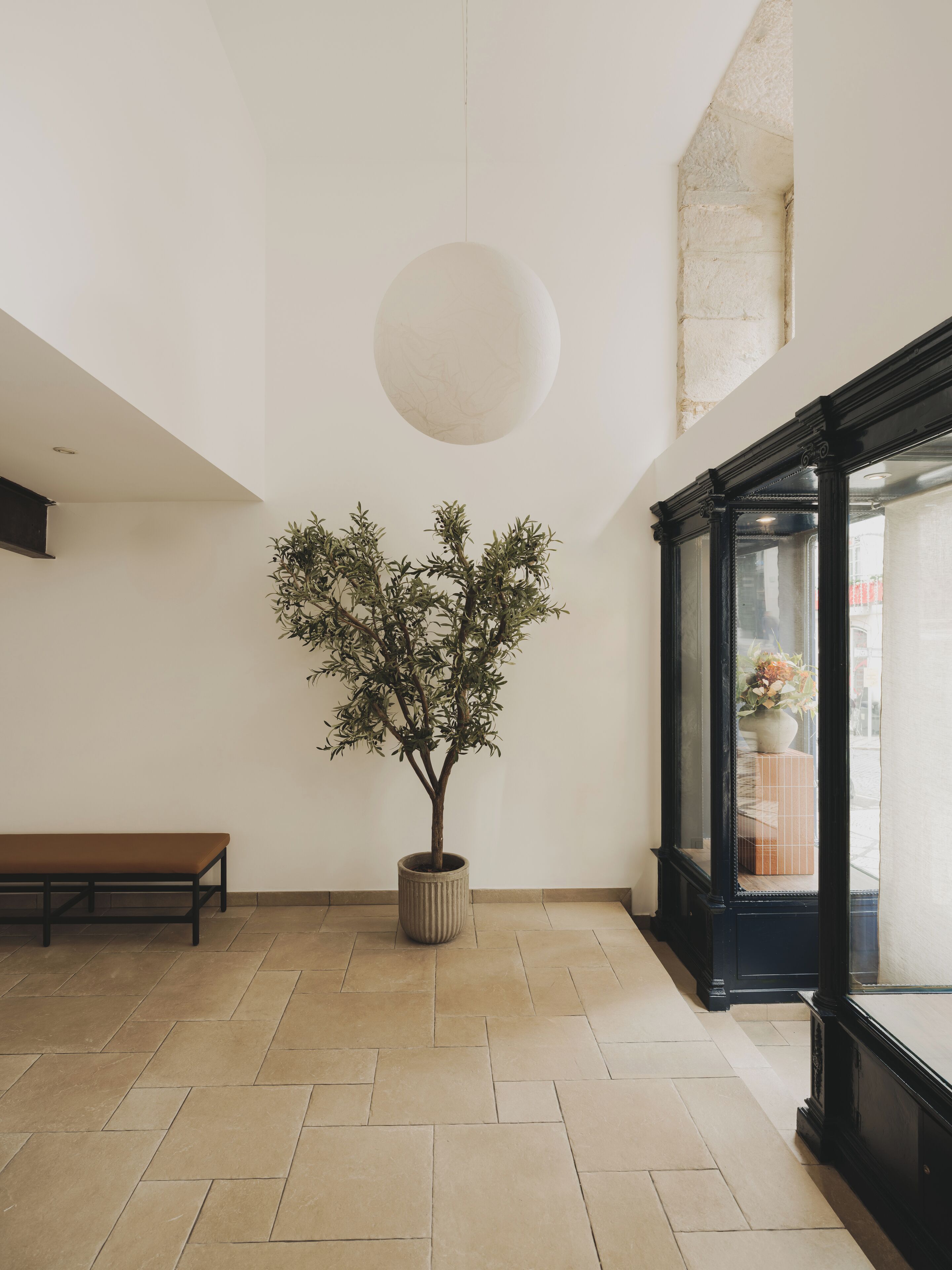Ein Zimmer mit einem großen Kübelbaum, einer Bank und einem großen Fenster mit Blick.