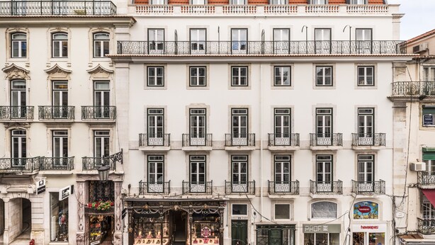 Un edificio de varios pisos con balcones, una fachada comercial con un letrero y una tienda con un escaparate lleno de flores.