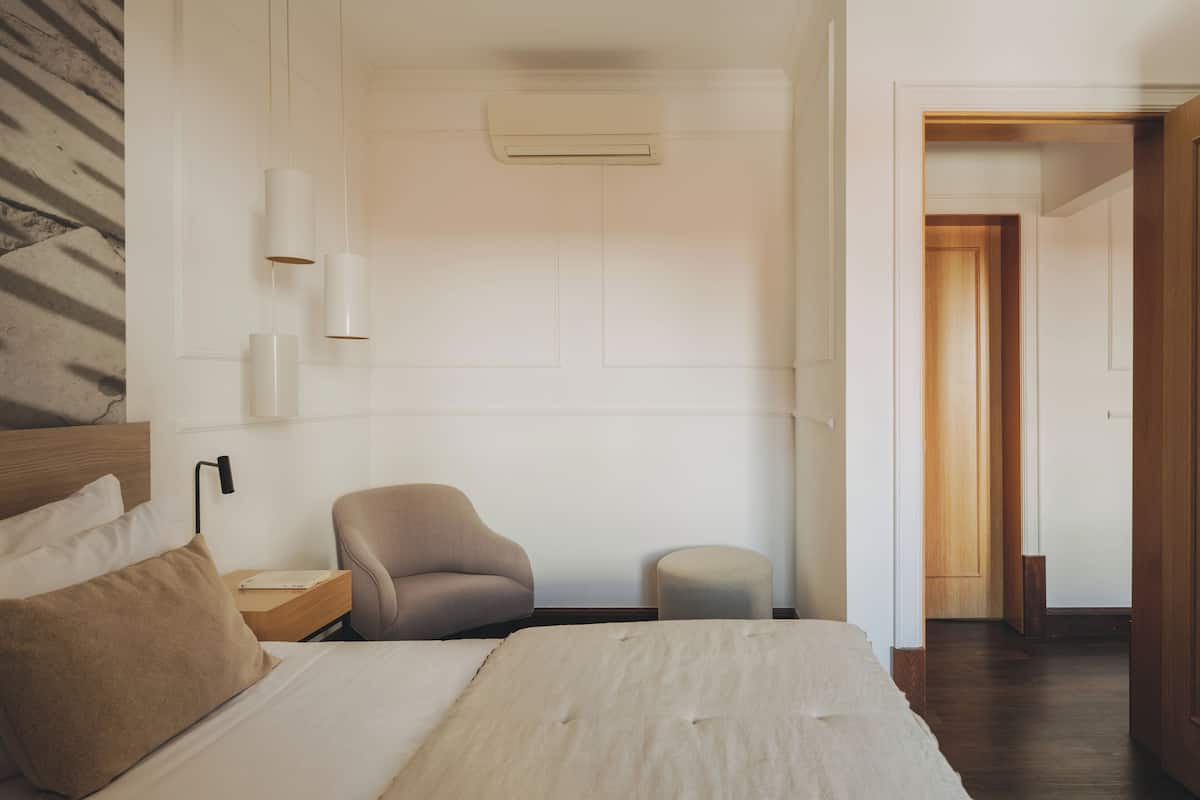 Een slaapkamer met een bed, een stoel, een nachtkastje en een klein krukje.