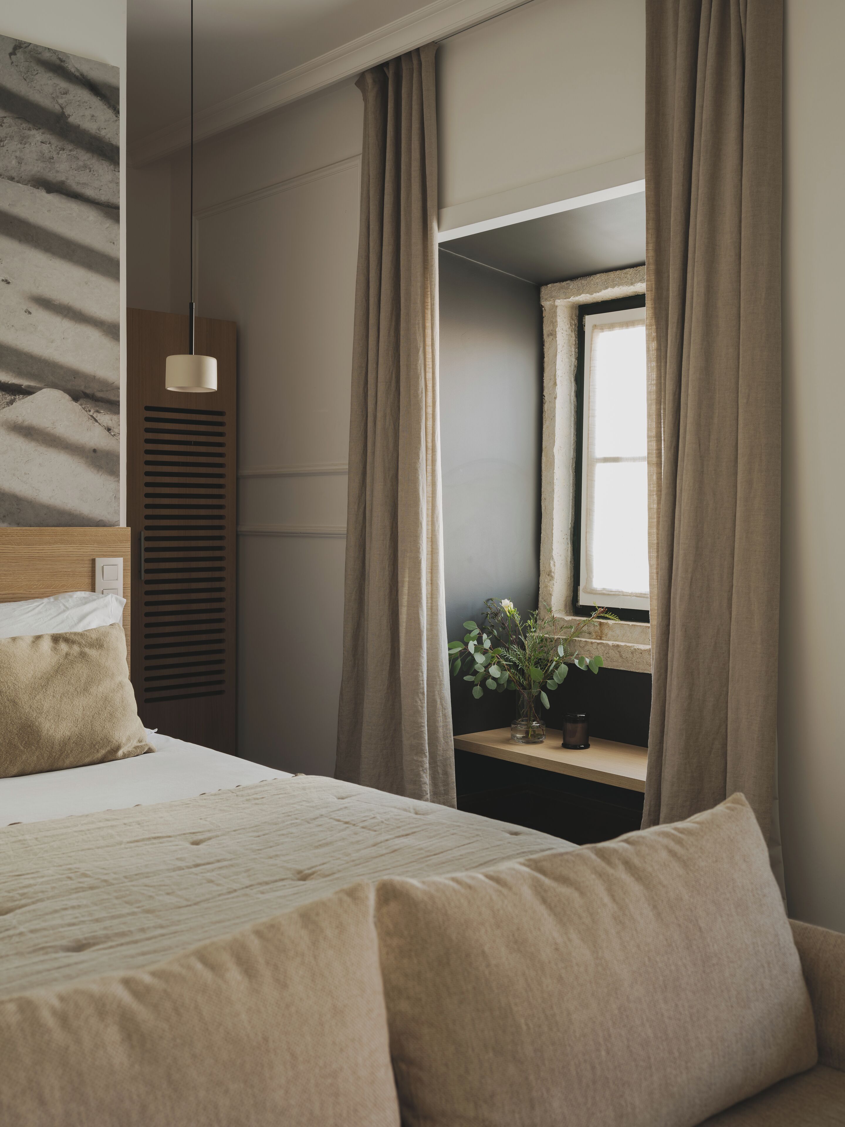 Une chambre à coucher avec un lit, une table de chevet ornée d’une plante et une fenêtre avec des rideaux.