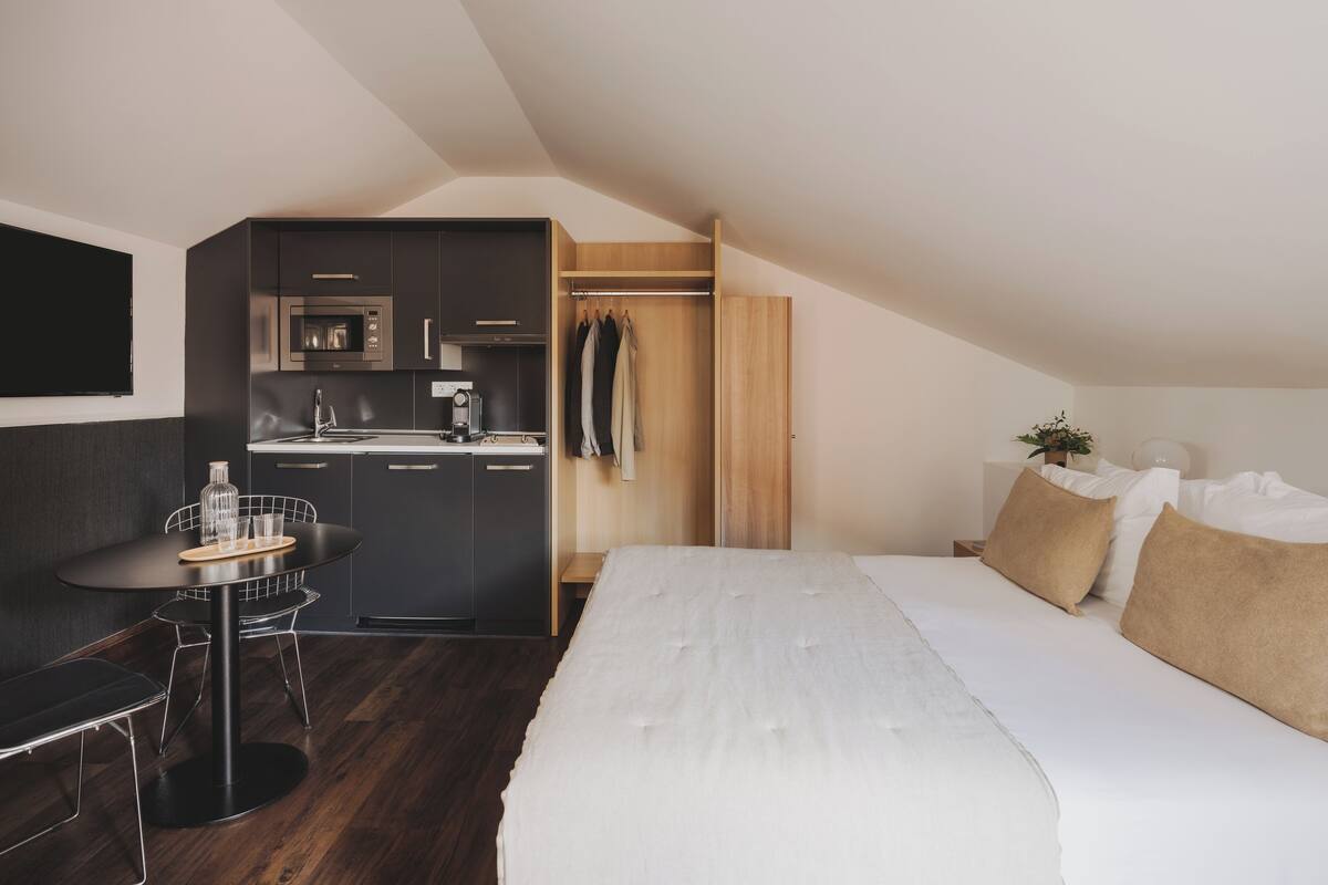 Een compacte, moderne kamer met een kitchenette, een eethoek en een bed.