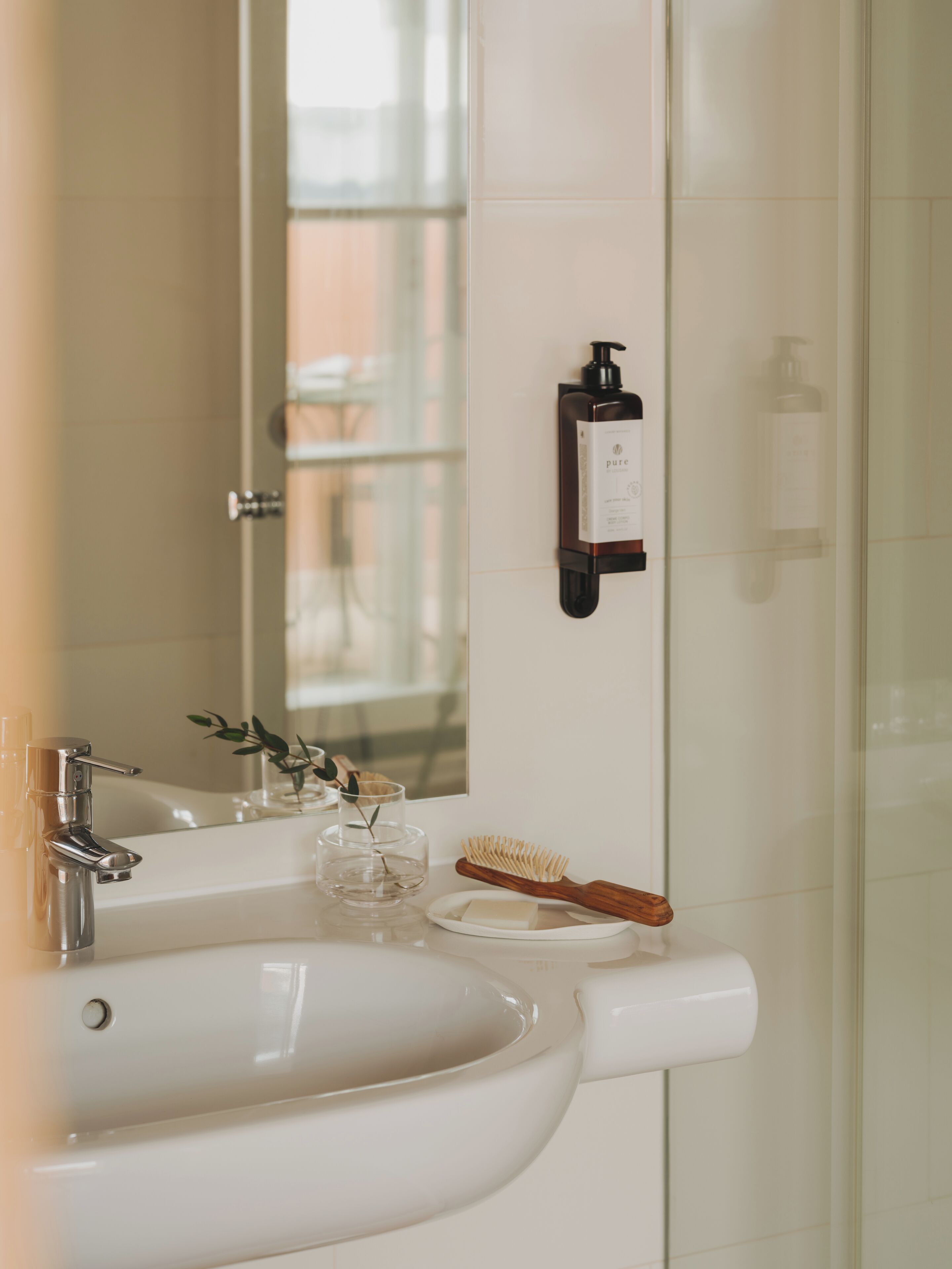 A bathroom with a white sink, a mirror, and a wall-mounted soap dispenser.