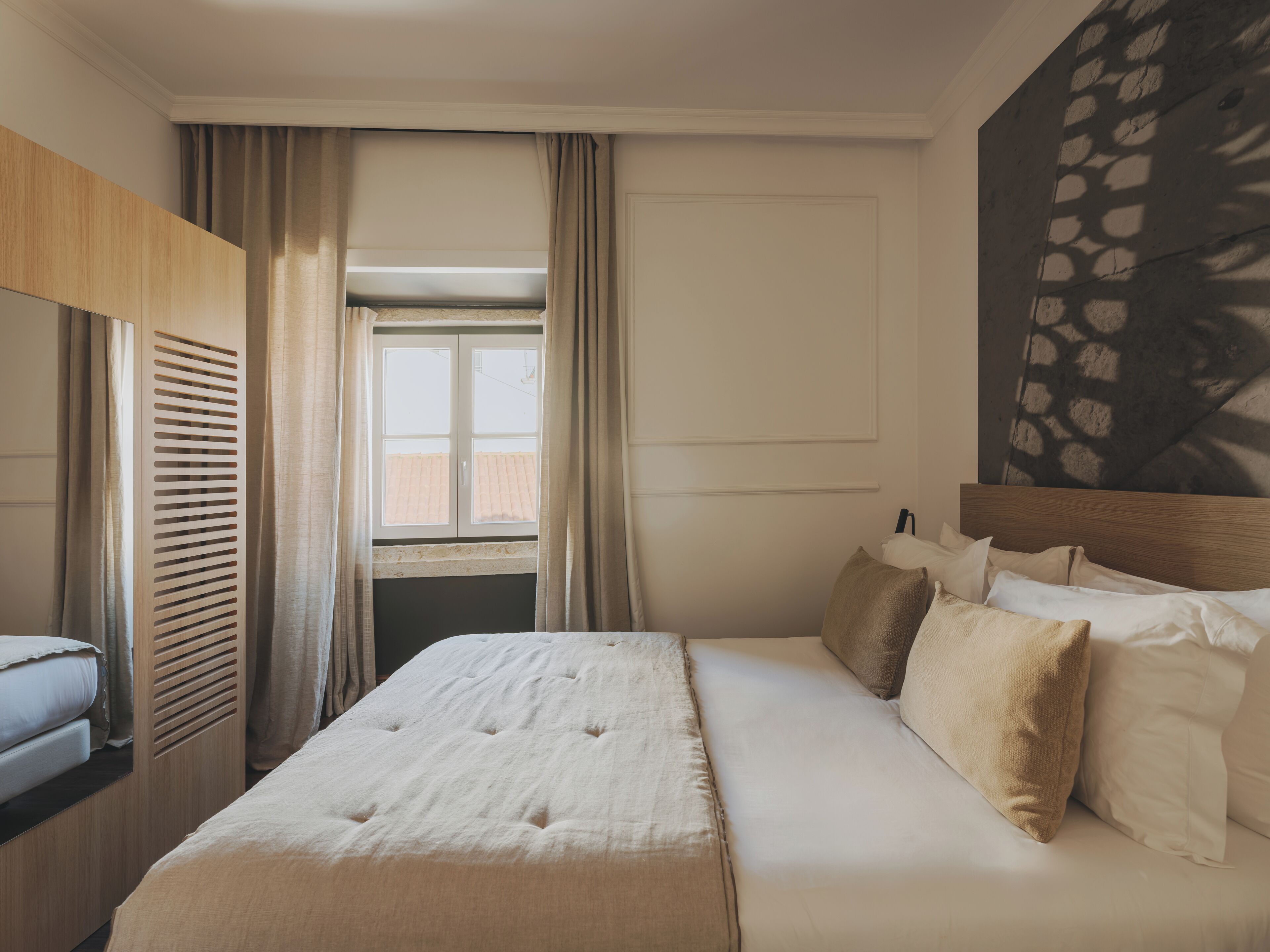 Una habitación de hotel con cama, cabecera de madera, ventana con cortinas y pared con diseño geométrico.