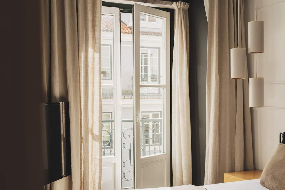 Een hotelkamer met een bed, een televisie, een raam met gordijnen en uitzicht op een balkon.