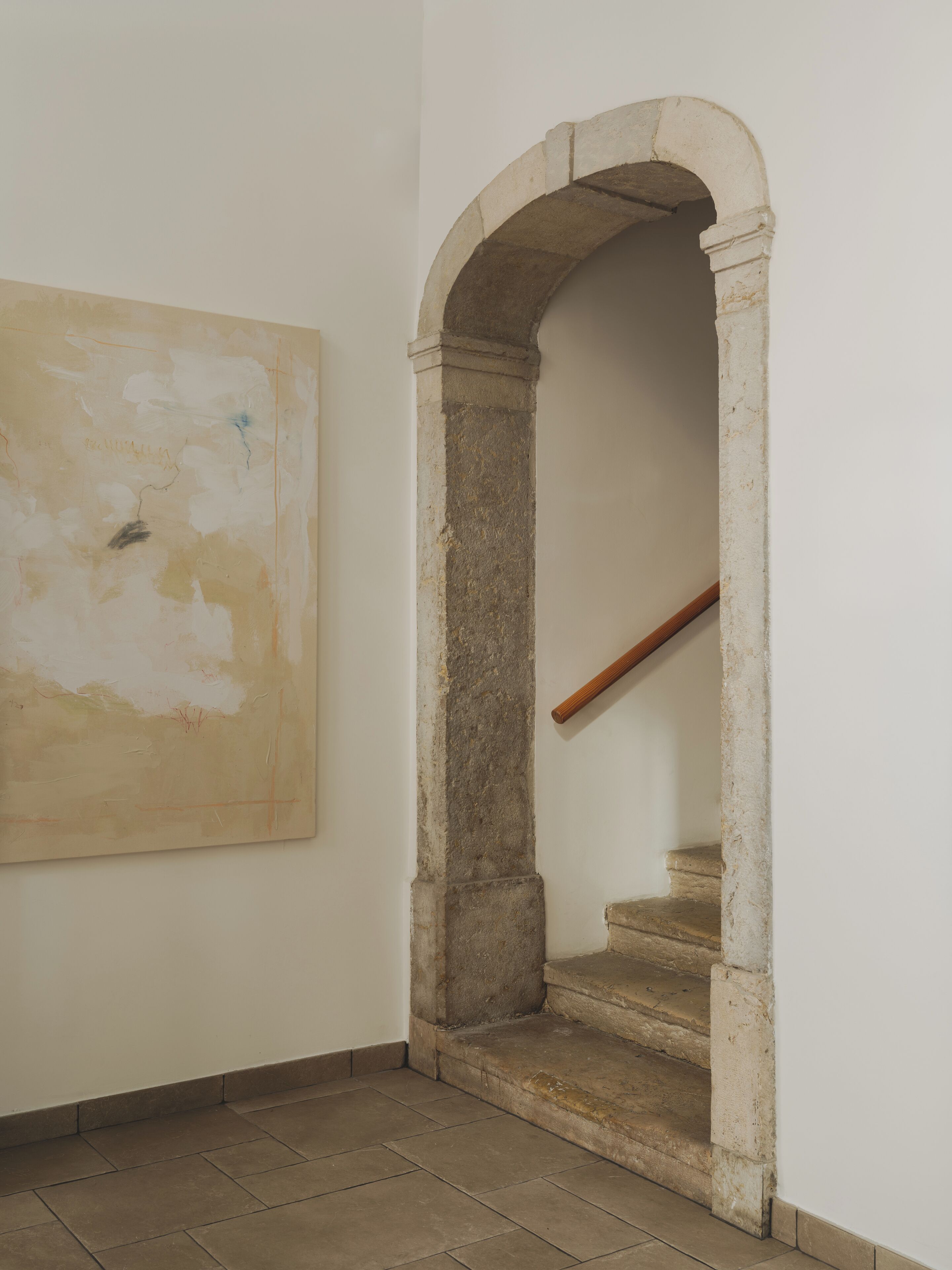A hallway with a stone staircase, a white wall, and a large abstract painting.