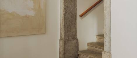 A hallway with a stone staircase, a white wall, and a large abstract painting.