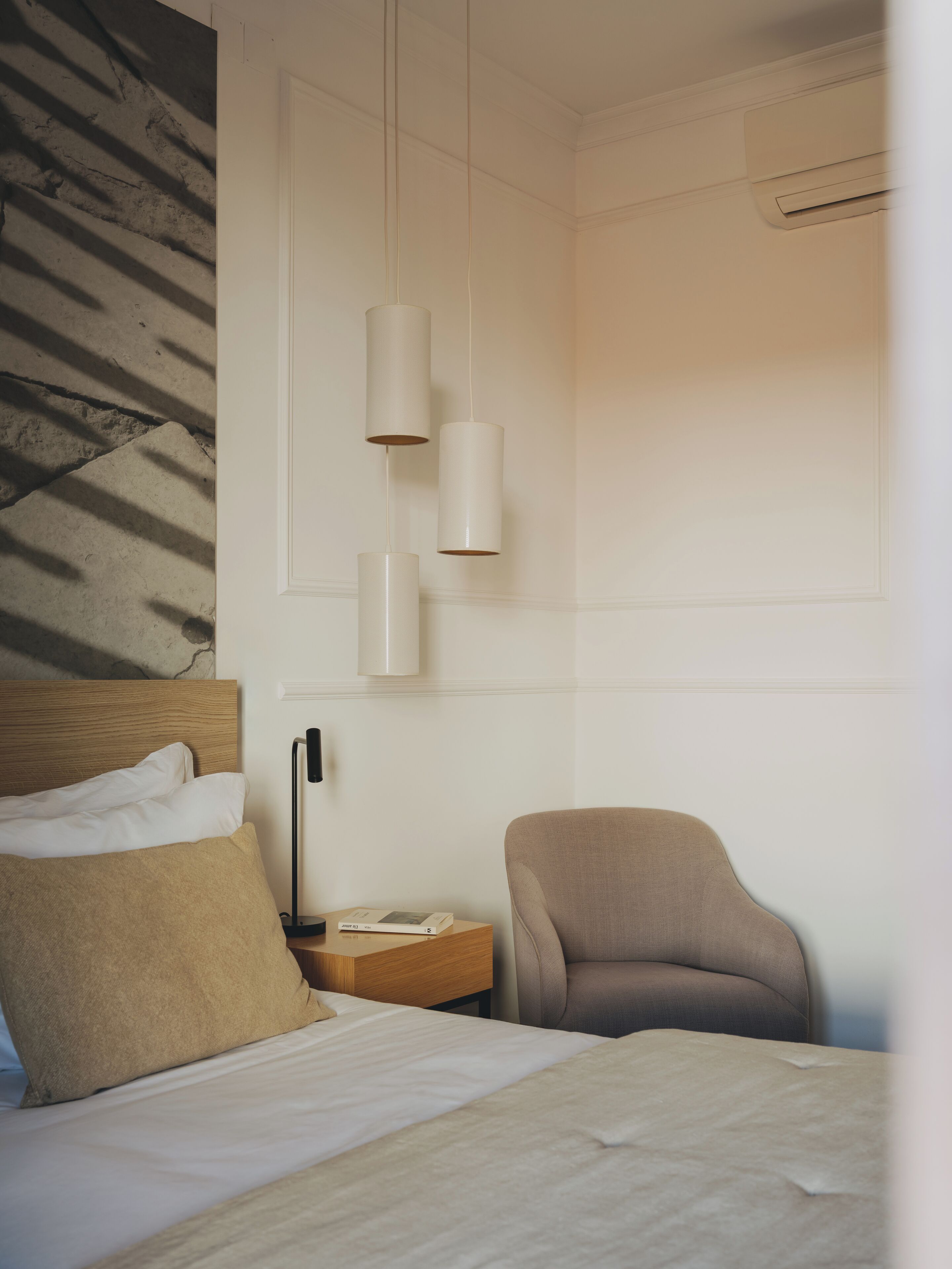 A hotel room with a bed, a chair, a nightstand, and a wall-mounted lamp.