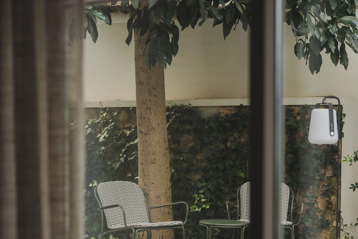 Uitzicht door een raam op een patio met een boom, een bank en een tafel.