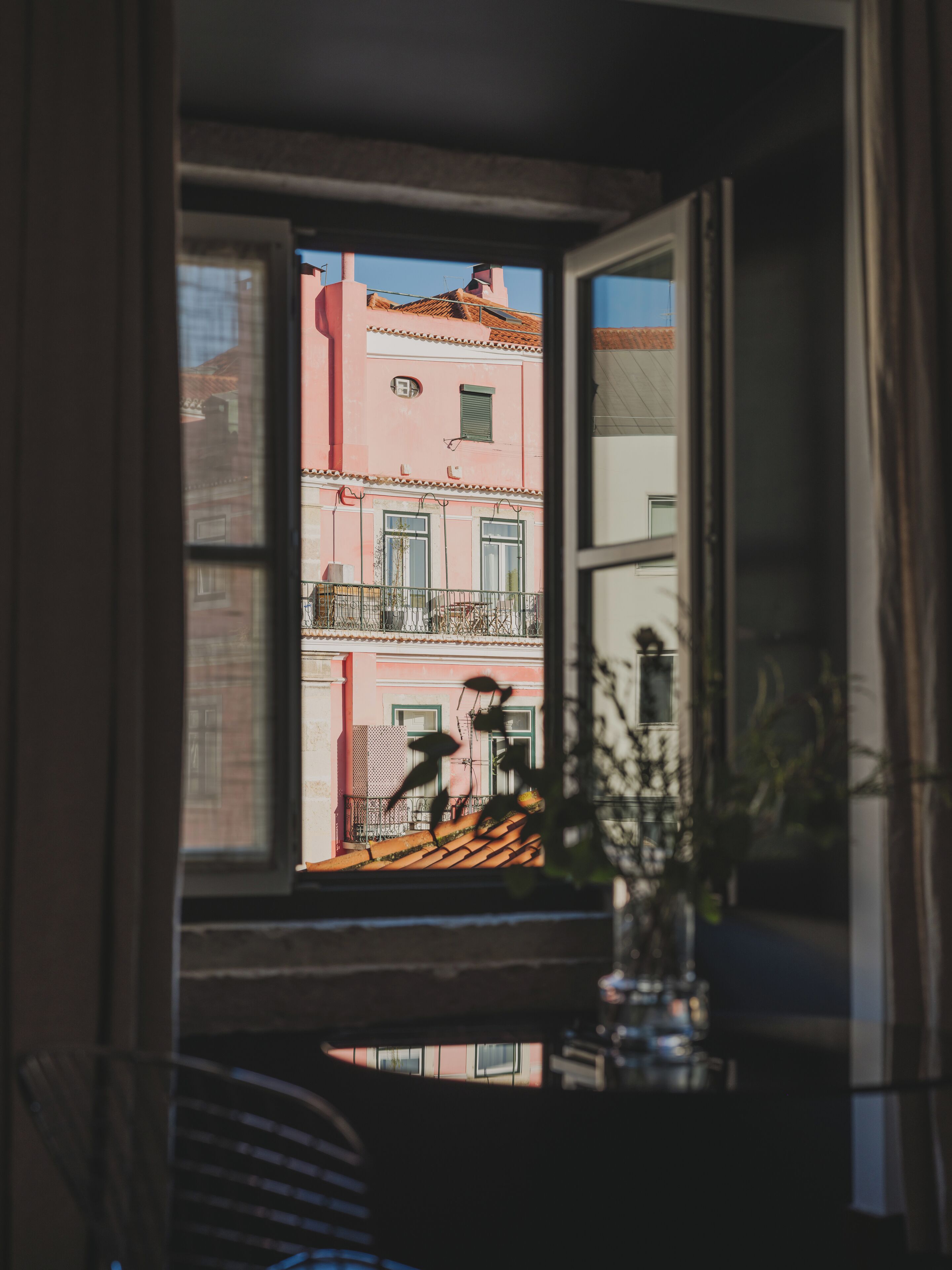 A window with a view of a pink building with balconies and a tiled roof.