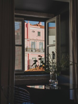 Uma janela com vista para um edifício rosa com varandas e telhado em telhas.