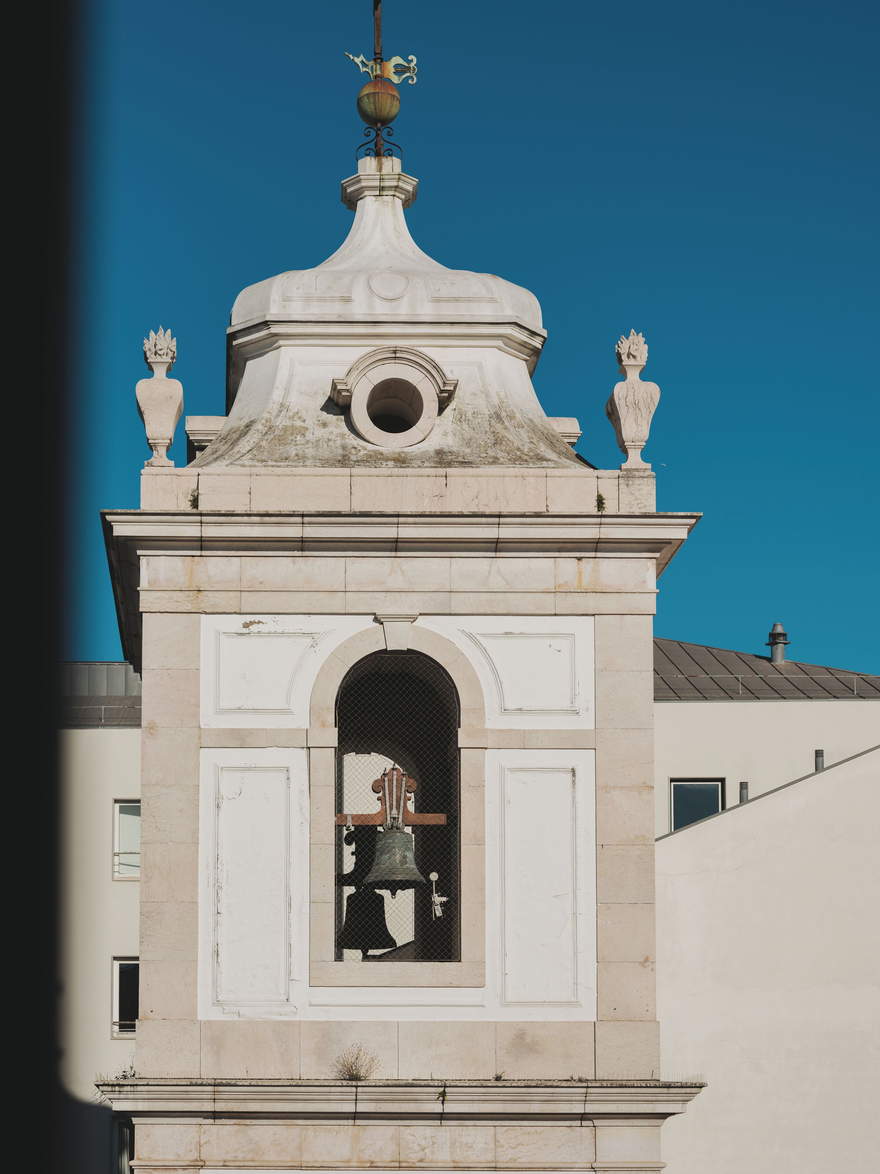 Una torre de campanas con veleta, un vano circular y una estatua en la parte superior.