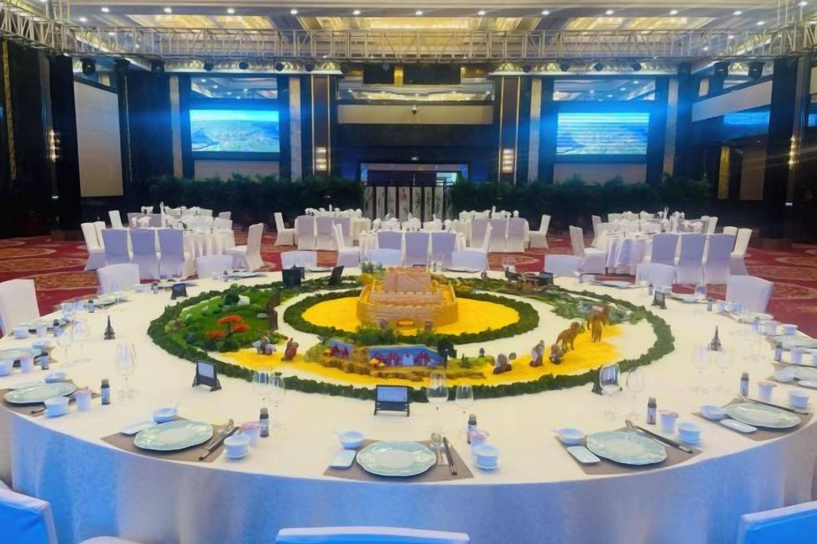 Une salle de banquet avec des tables rondes, des chaises blanches et une composition florale centrale.