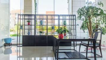 A modern interior with a glass table, black chairs, and a metal plant stand with potted plants.
