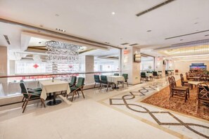 Une salle à manger d’hôtel avec des tables et des chaises, un lustre et un tapis à motifs.