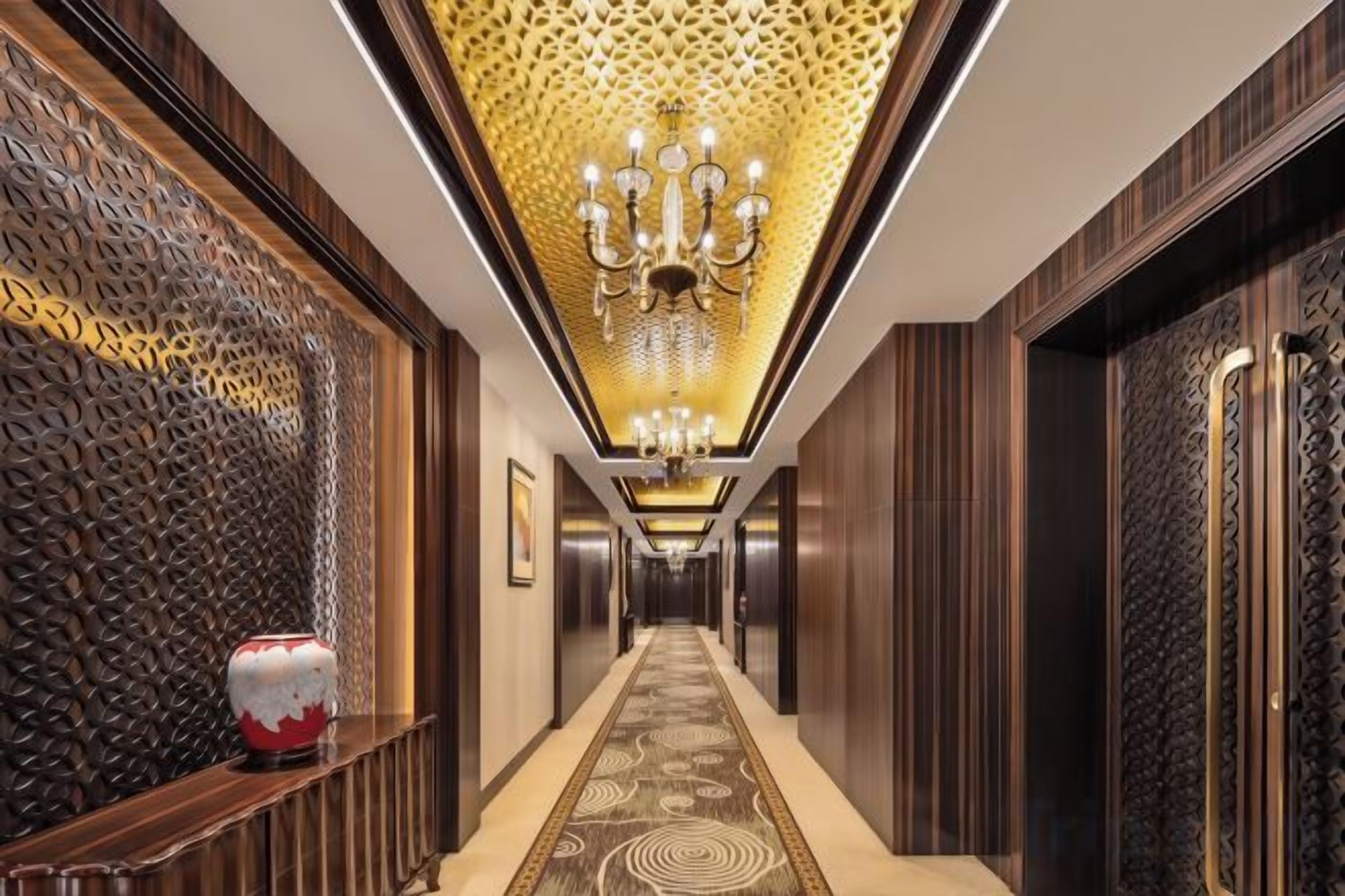 A hallway with a patterned carpet, a chandelier, and a decorative wall.