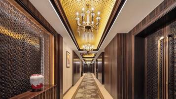 A hallway with a patterned carpet, a chandelier, and a decorative wall.