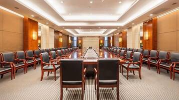 A conference room with a long table and rows of chairs, equipped with a projector screen at the front.