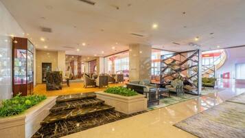 A hotel lobby with a reception desk, seating area, and a staircase.