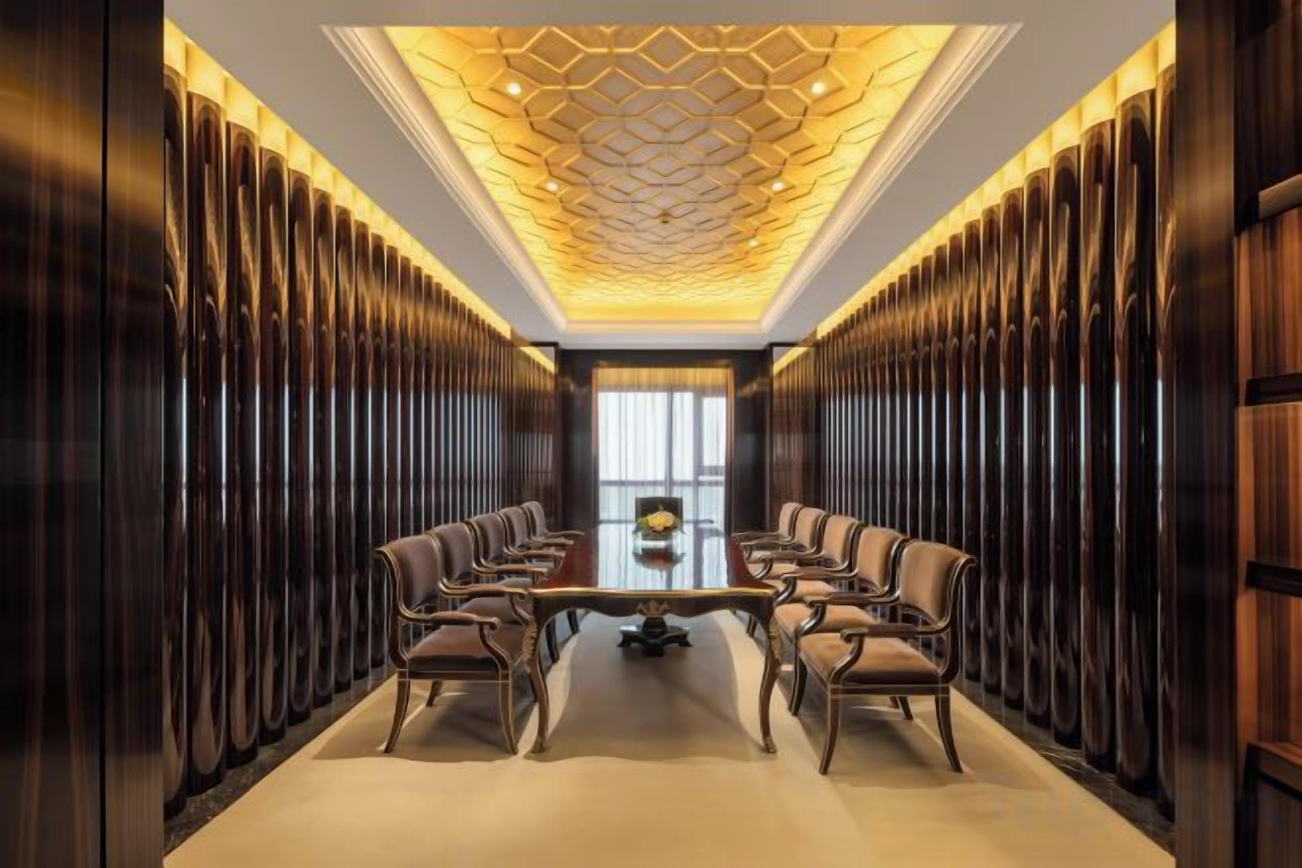 A conference room with a long table and chairs, wooden paneling on the walls, and a patterned ceiling.