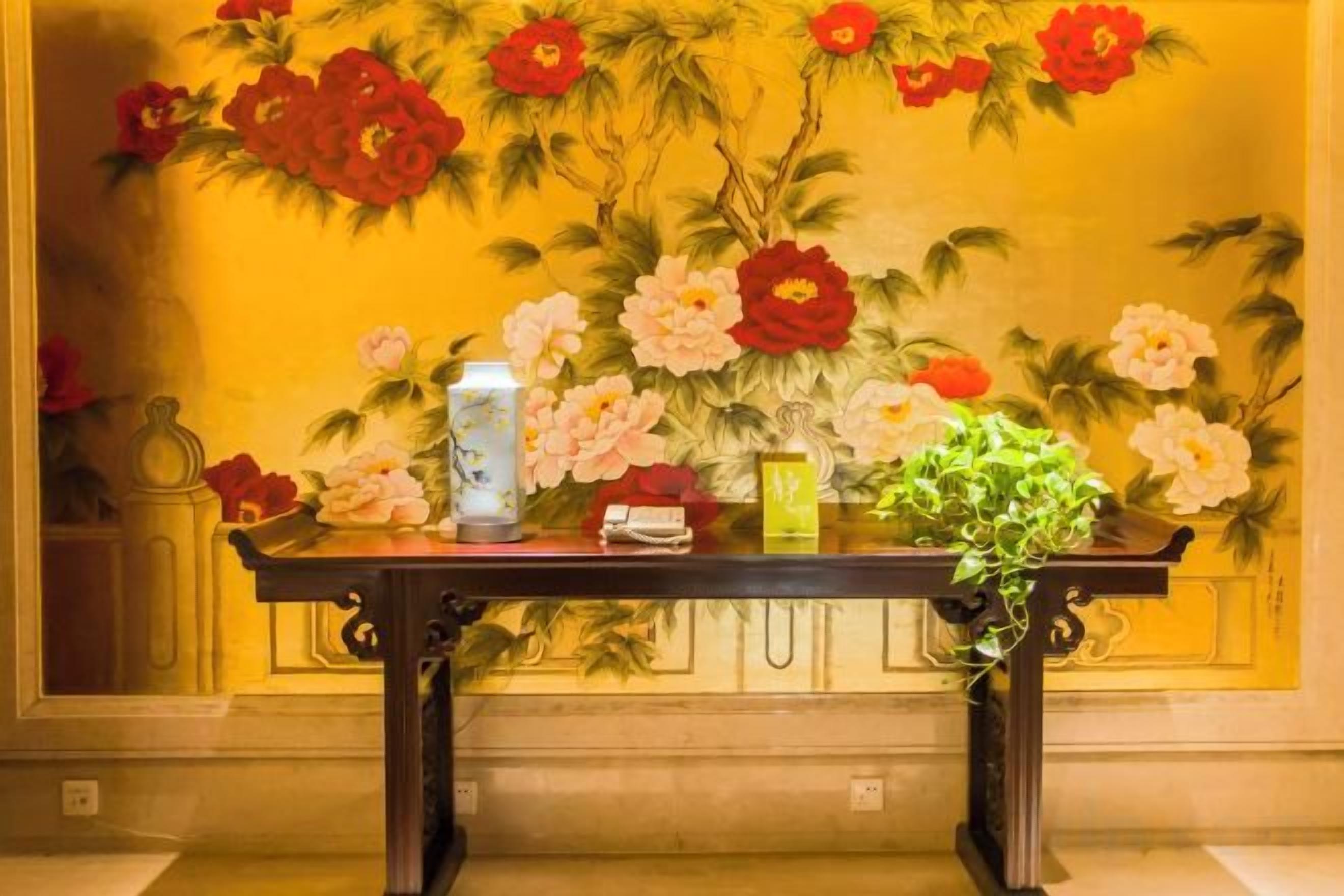 A table with a vase, a bottle, and a plant in front of a floral mural.