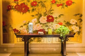 Une table avec un vase, une bouteille et une plante, le tout placé devant une fresque florale.