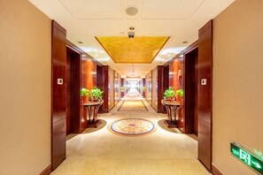 A hotel hallway with wooden doors, potted plants, a patterned carpet, and a green exit sign. - Petroleum Hotel (Yulin)