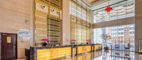 A spacious lobby with a reception desk, large windows, and a high ceiling.