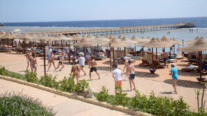 Une plage avec des chaises longues, des parasols et une jetée qui s’avance dans la mer.