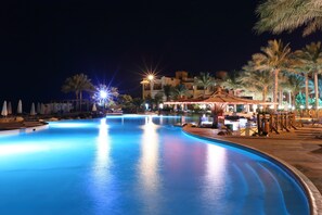A nighttime swimming pool with illuminated edges, palm trees, and a building with traditional architecture in the background. - Rehana Royal Prestige & Spa - All Inclusive (Sharm El Sheikh)