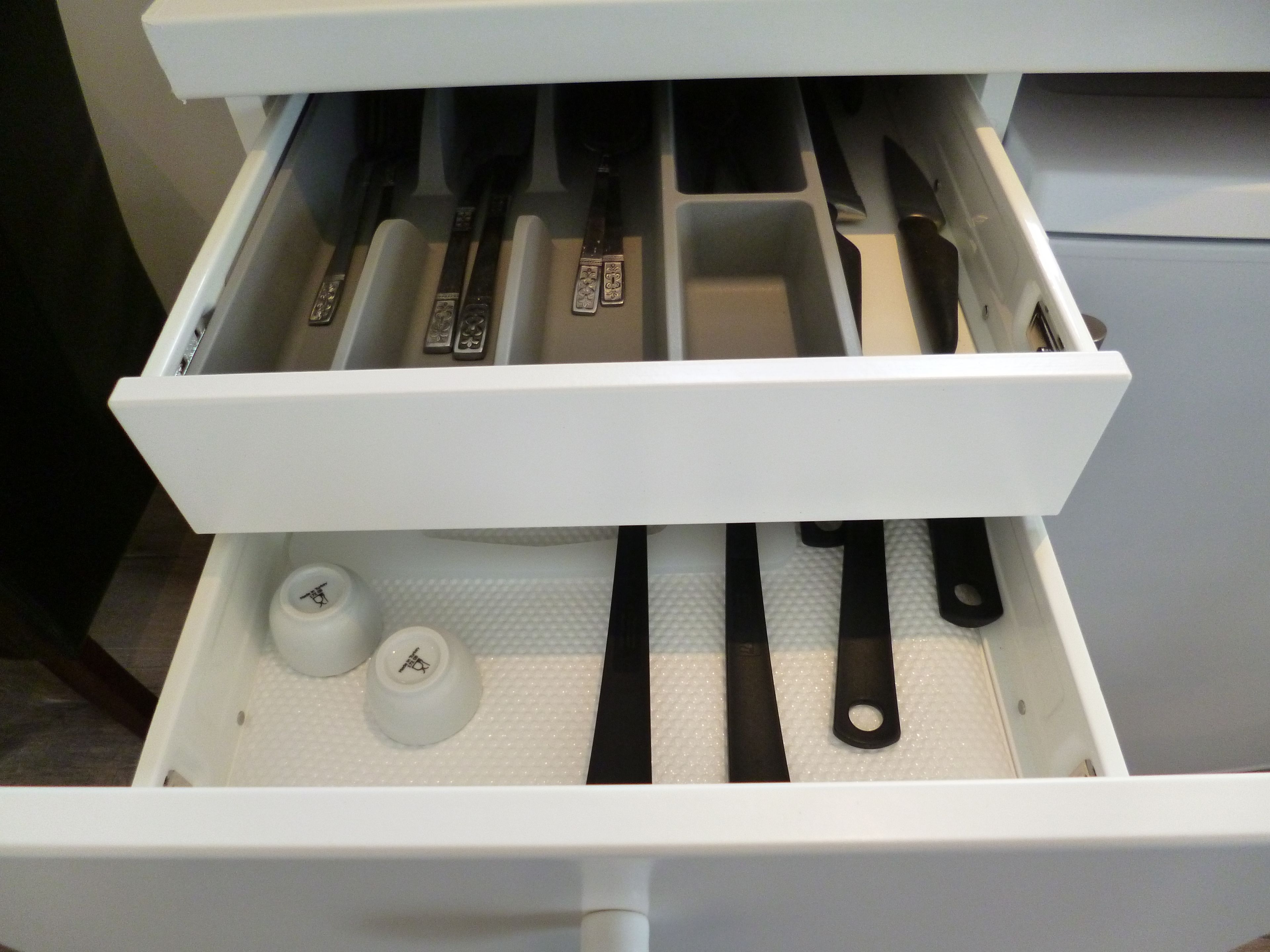 Eine Schublade mit verschiedenen Küchenutensilien und Behältern, darunter Messer und eine kleine Flasche.
