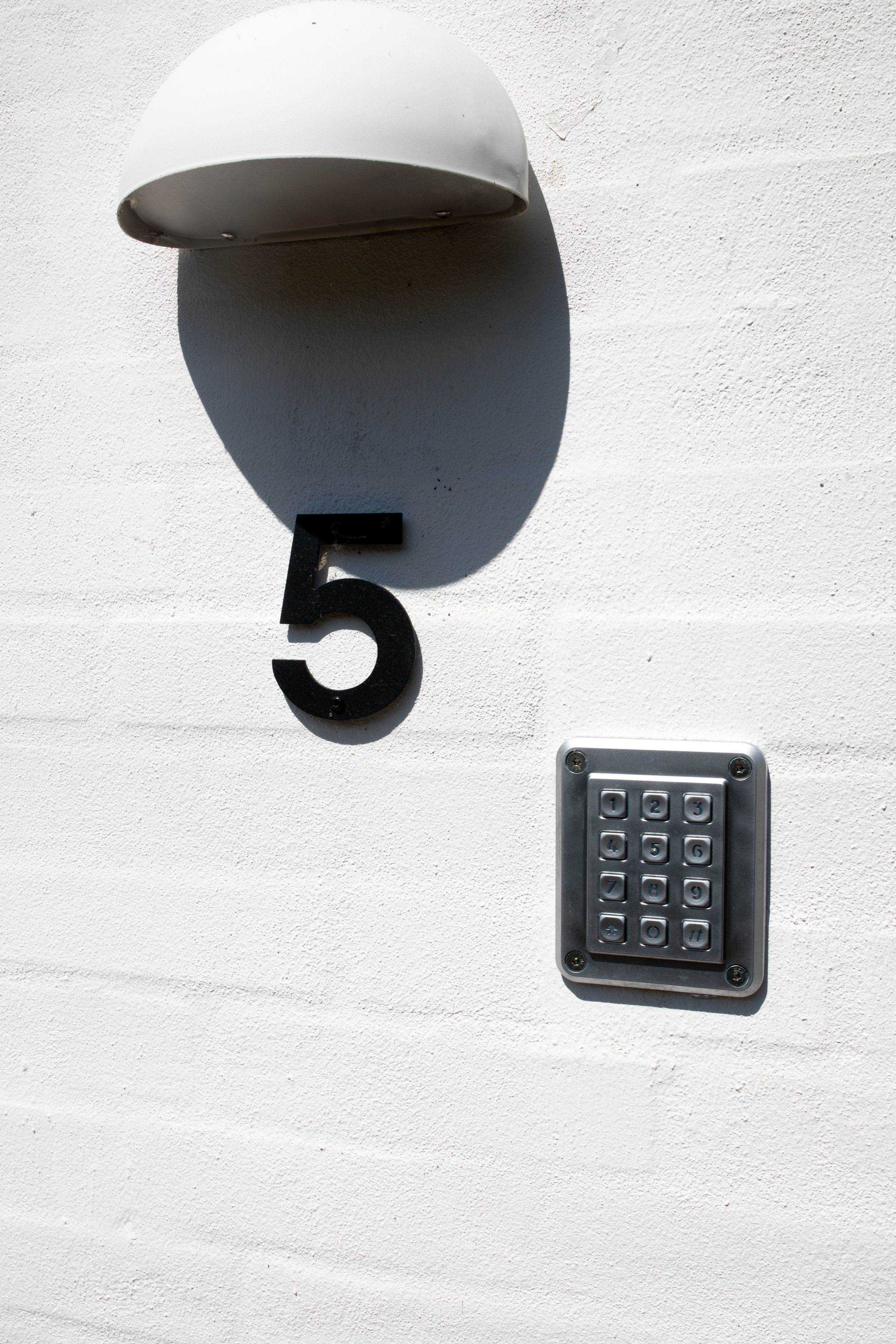 Un numéro de maison, le chiffre « 5 », et un clavier numérique sur un mur blanc.