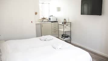 Habitació d'hotel amb un llit, una cuineta petita, un televisor fixat a la paret i una finestra amb persianes.