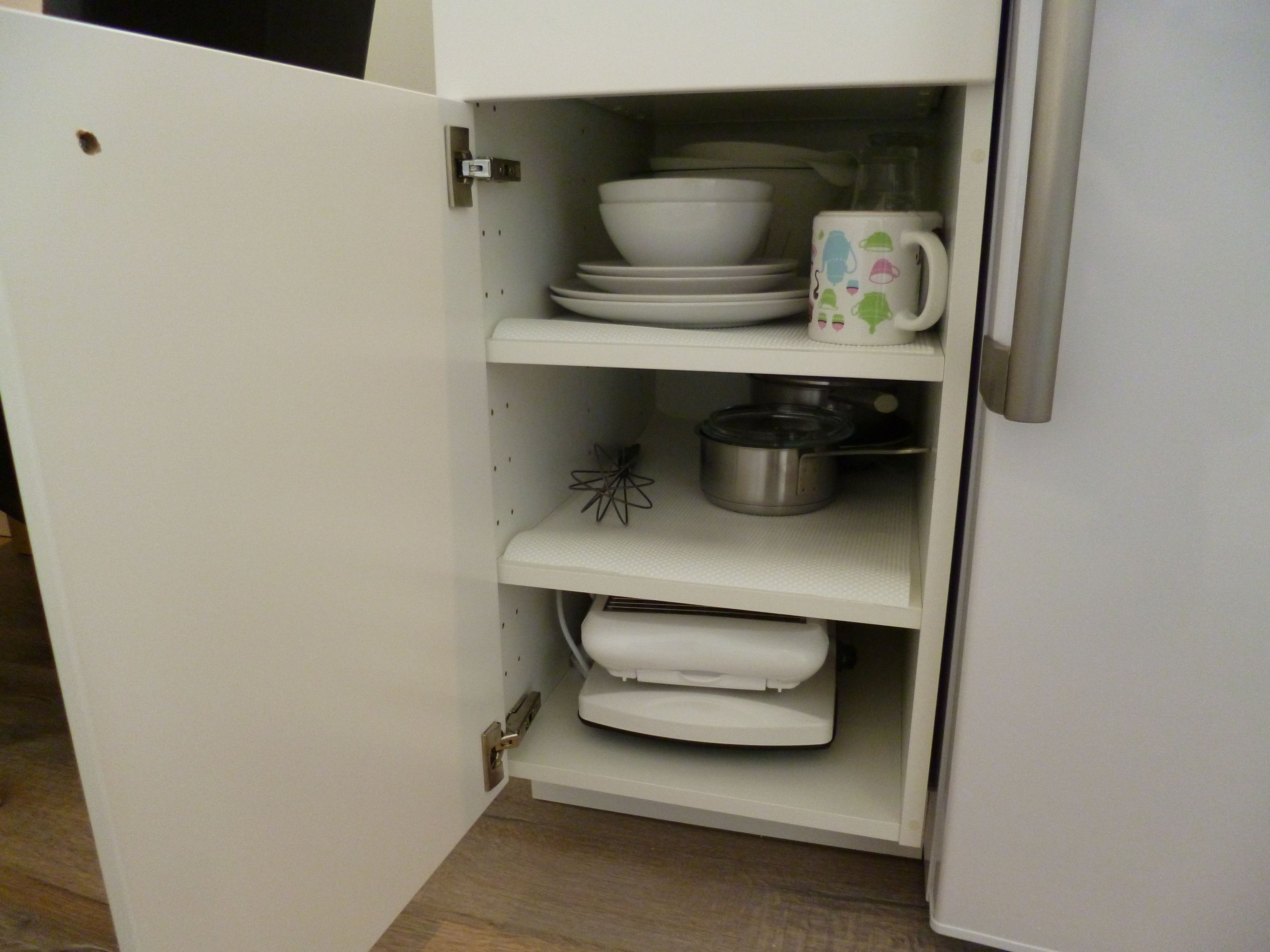 A white kitchen cabinet with shelves holding white dishes, a white mug, and a stainless steel pot.