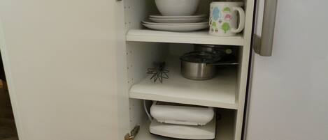 A white kitchen cabinet with shelves holding white dishes, a white mug, and a stainless steel pot.